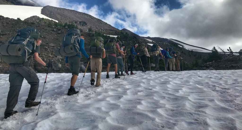 a group of outward bound students carrying backpacks hike across a snowy field on an expedition in oregon